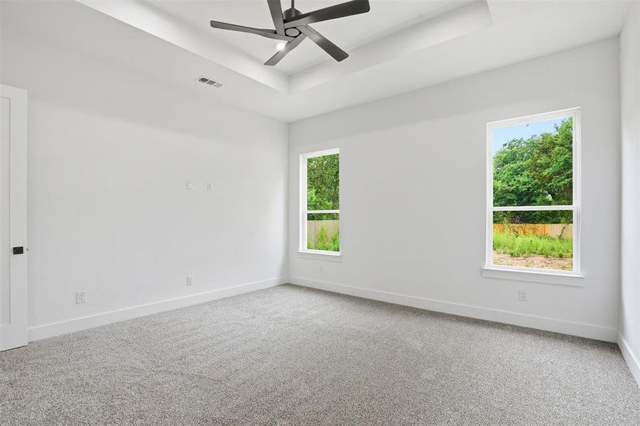 Spacious room featuring a contemporary ceiling fan, tray ceiling, two large windows, and plush grey carpeting