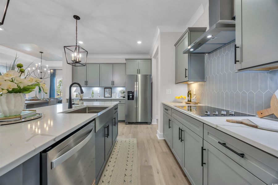 Kitchen with appliances with stainless steel finishes, gray cabinetry, light wood-style floors, wall chimney range hood, and decorative light fixtures