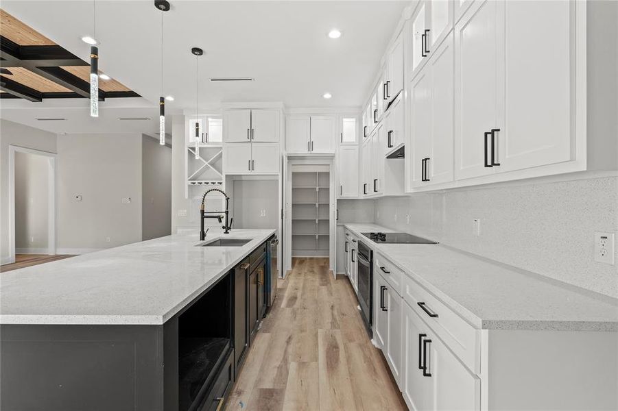 Kitchen featuring sink, an island with sink, pendant lighting, light hardwood / wood-style floors, and white cabinets