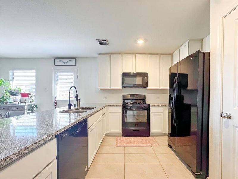 Kitchen with black appliances, white cabinets, light stone countertops, light tile patterned flooring, and recessed lighting