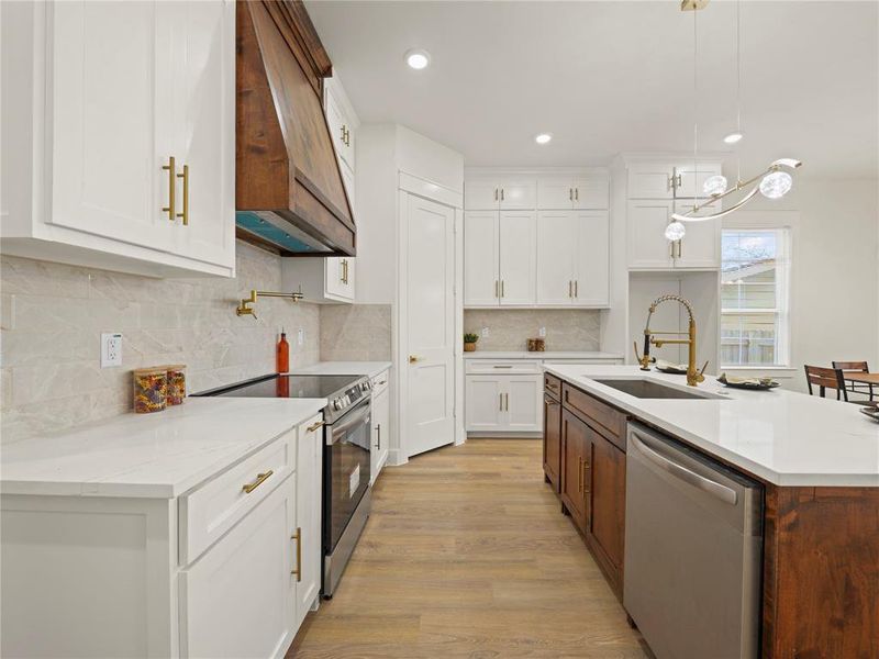 Dual tone kitchen with stainless steel appliances, two tone cabinets, an island with sink, light wood-style flooring, and light stone counters