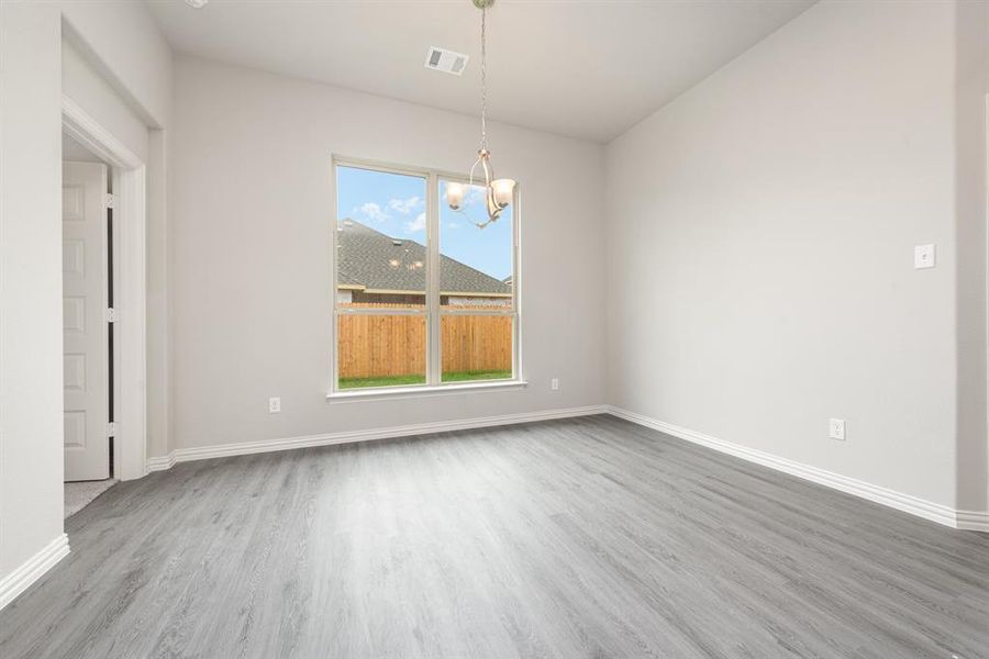 Unfurnished room with wood-type flooring, a notable chandelier, and a wealth of natural light