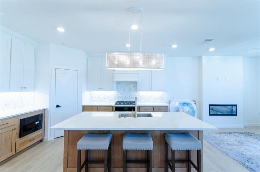 Kitchen with light wood-style flooring, a kitchen island with sink, backsplash, a breakfast bar area, and pendant lighting