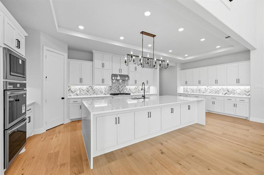 Kitchen with a raised ceiling, decorative backsplash, a large island, white cabinets, and recessed lighting