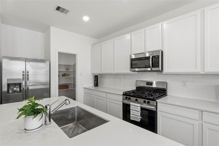 Modern kitchen featuring quartz countertops, stainless steel appliances, gas range, and ample cabinet space.
