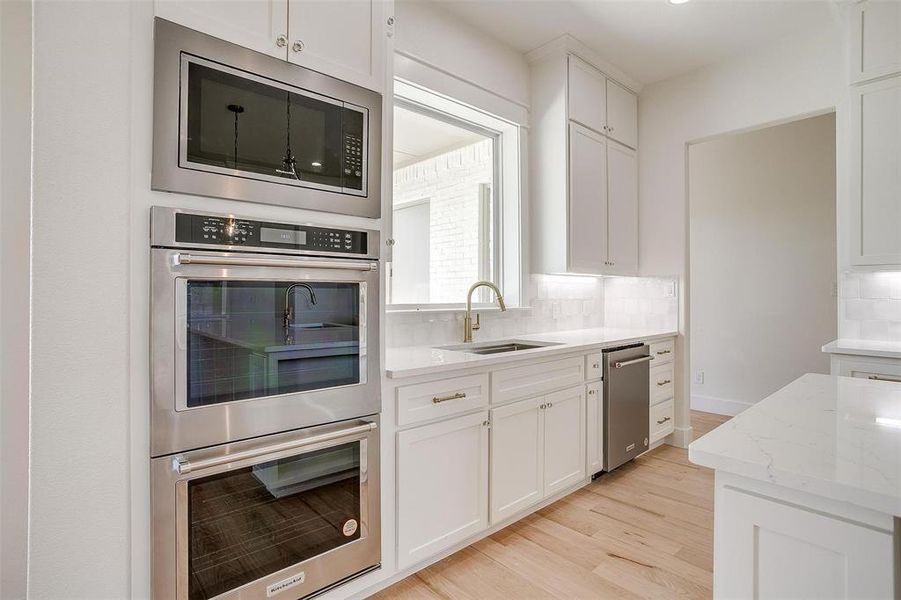 Kitchen featuring appliances with stainless steel finishes, a sink, decorative backsplash, light wood finished floors, and white cabinets