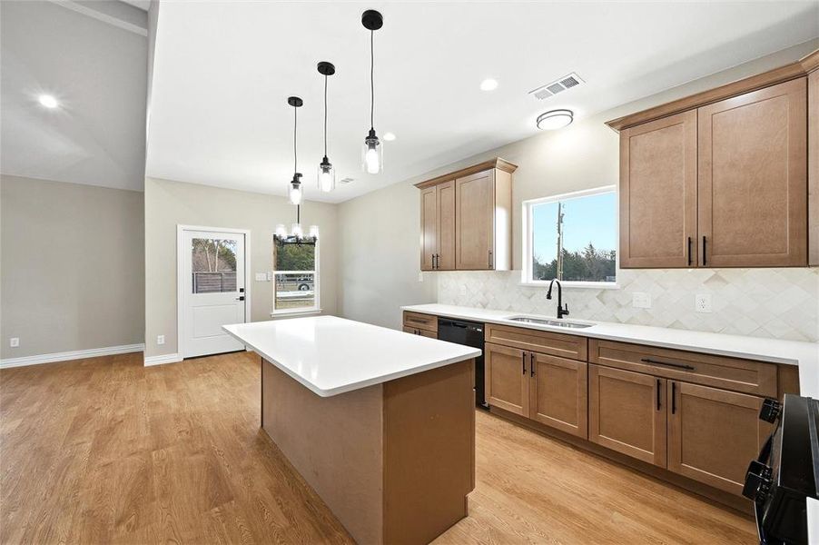 Kitchen with a kitchen island, wood finish cabinetry, black appliances, and light wood-style flooring Kitchen with a kitchen island, wood finish cabinetry, black appliances, and light wood-style flooring