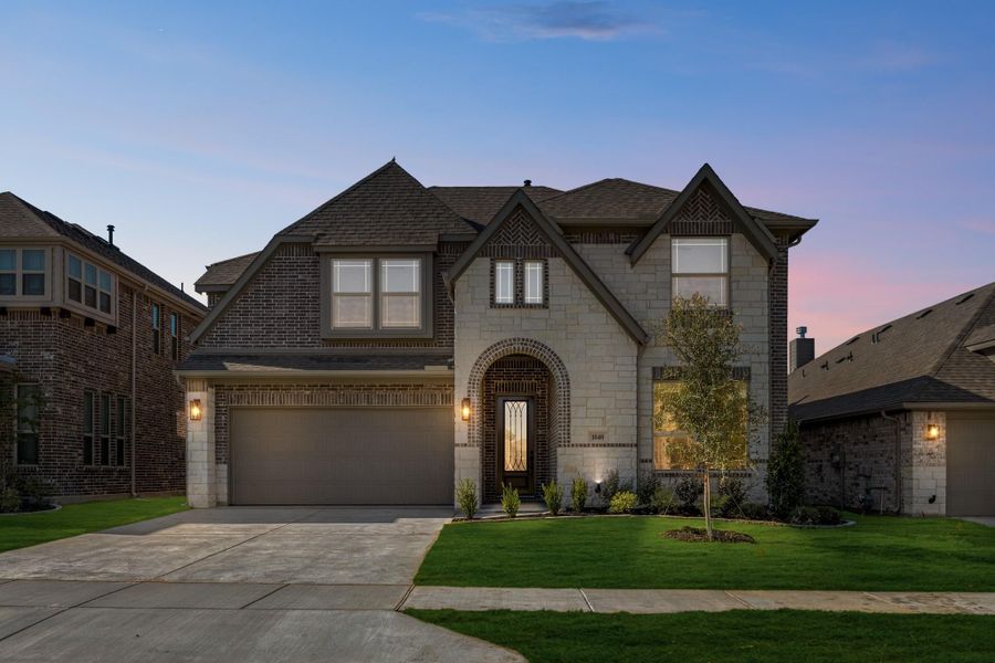 Two-story home with stone and brick exterior, arched entry, two-car garage, and manicured lawn at dusk Two-story home with stone and brick exterior, arched entry, two-car garage, and manicured lawn at dusk