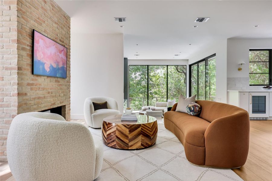 Spacious living area featuring a brick fireplace, built-in wet bar, wood-finish flooring, recessed lighting, and expansive floor-to-ceiling windows