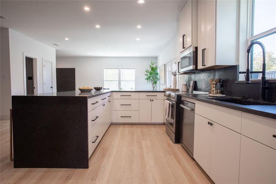 Kitchen featuring white cabinets, sink, light hardwood / wood-style floors, kitchen peninsula, and stainless steel appliances