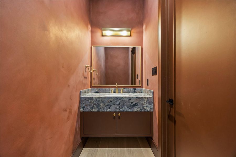 Rich lime washed walls create a dramatic backdrop for this designer powder bath, complemented by a floating vanity with a unique red quartzite countertop, an integrated sink, and warm brass fixtures. A bold, elevated space that leaves a lasting impression for guests.