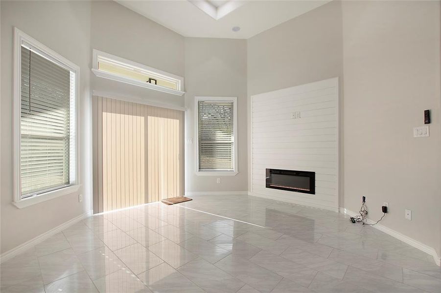 Unfurnished living room featuring plenty of natural light, a large fireplace, and a towering ceiling