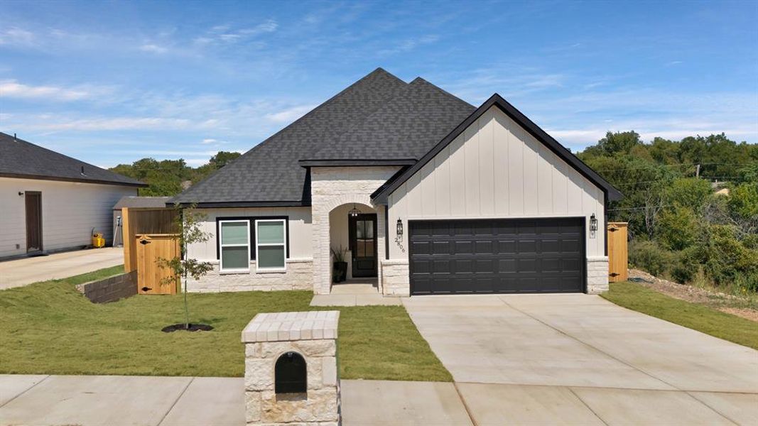 View of front of home with stone siding, roof with shingles, a front yard, concrete driveway, and board and batten siding View of front of home with stone siding, roof with shingles, a front yard, concrete driveway, and board and batten siding