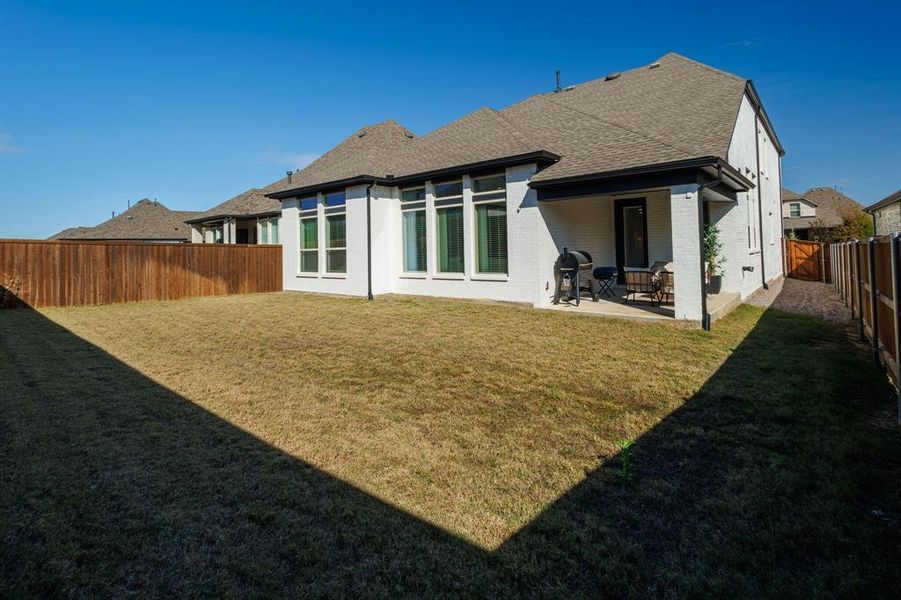 Rear view of house featuring brick siding, a shingled roof, a fenced backyard, and a patio area