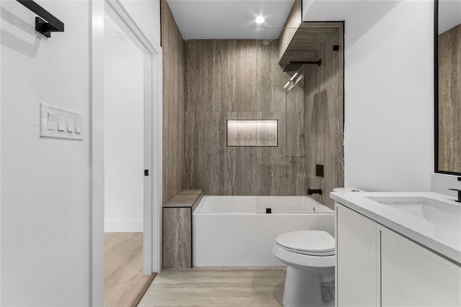 Contemporary bathroom featuring a tub and shower combination with full-height stone-look tile surround, a built-in bench, and an illuminated shower niche Contemporary bathroom featuring a tub and shower combination with full-height stone-look tile surround, a built-in bench, and an illuminated shower niche