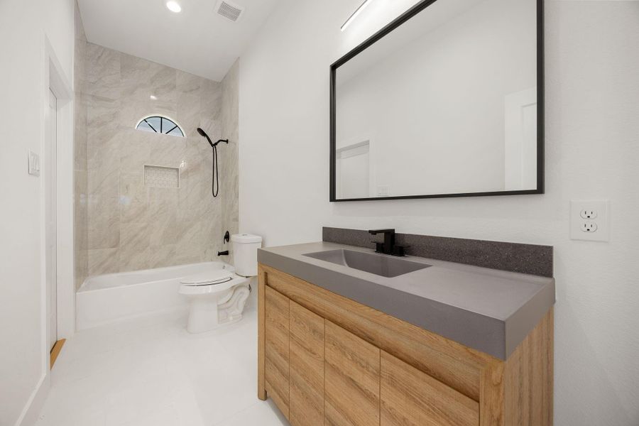 The primary bath features a quartz countertop vanity, large mirror, modern fixtures, and convenient tub and shower combination.