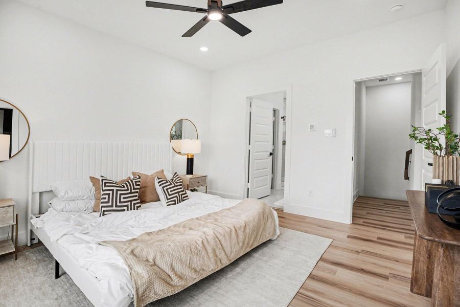 Bright and modern primary bedroom with large windows, wood flooring, and a ceiling fan, creating an inviting atmosphere.