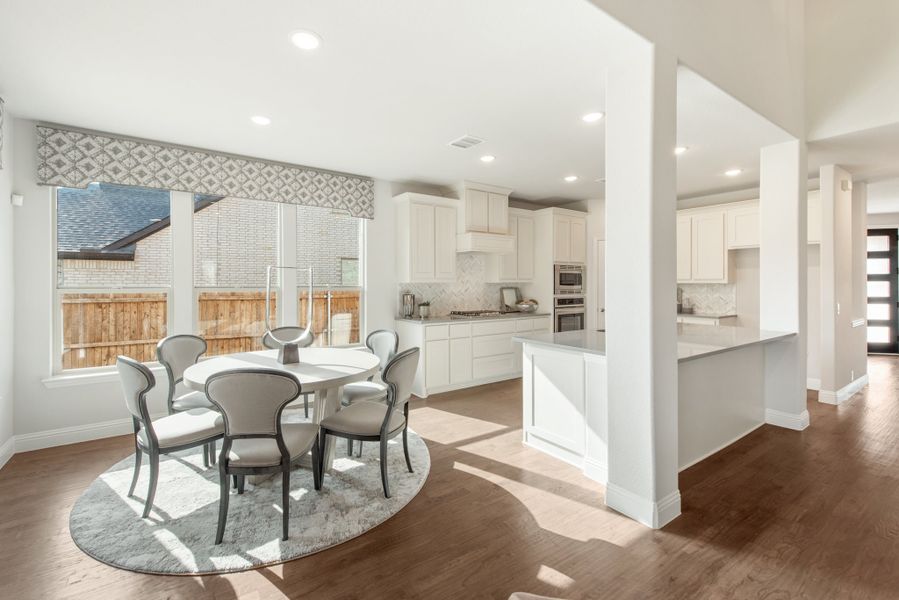 Open dining area with round table and six chairs, adjacent to white kitchen with hardwood floors