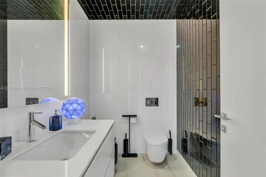 Modern vanity with a seamless integrated sink and countertop, wall-mounted toilet, floor-to-ceiling white wall tile, and black vertical glass subway tile accent walls Modern vanity with a seamless integrated sink and countertop, wall-mounted toilet, floor-to-ceiling white wall tile, and black vertical glass subway tile accent walls
