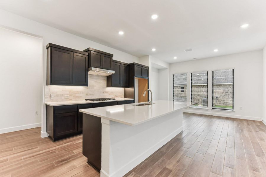 Kitchen with backsplash, wood finish floors, a kitchen island with sink, light stone countertops, and recessed lighting Kitchen with backsplash, wood finish floors, a kitchen island with sink, light stone countertops, and recessed lighting