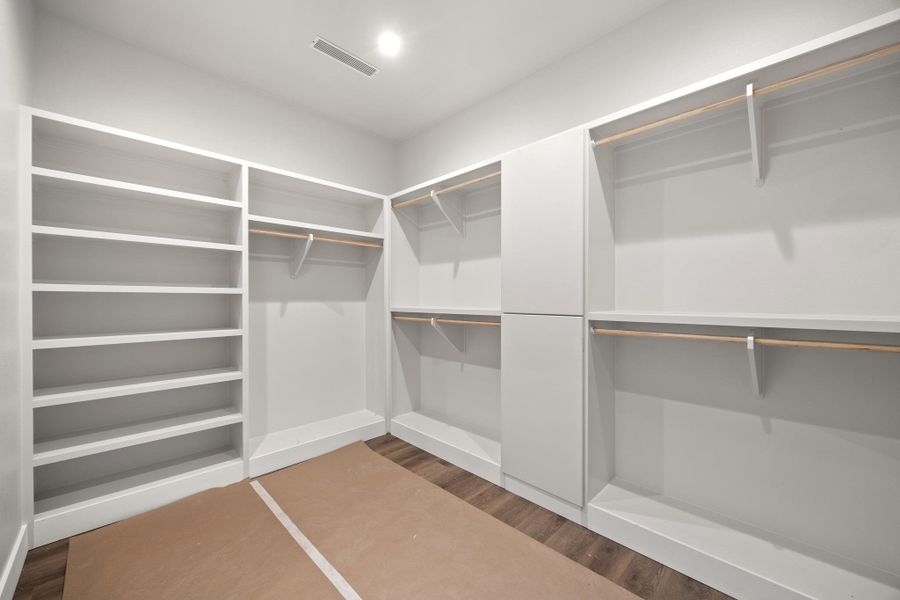Spacious walk-in closet featuring extensive built-in shelving, multiple hanging rods, closed cabinetry, wood-finish flooring, and recessed lighting