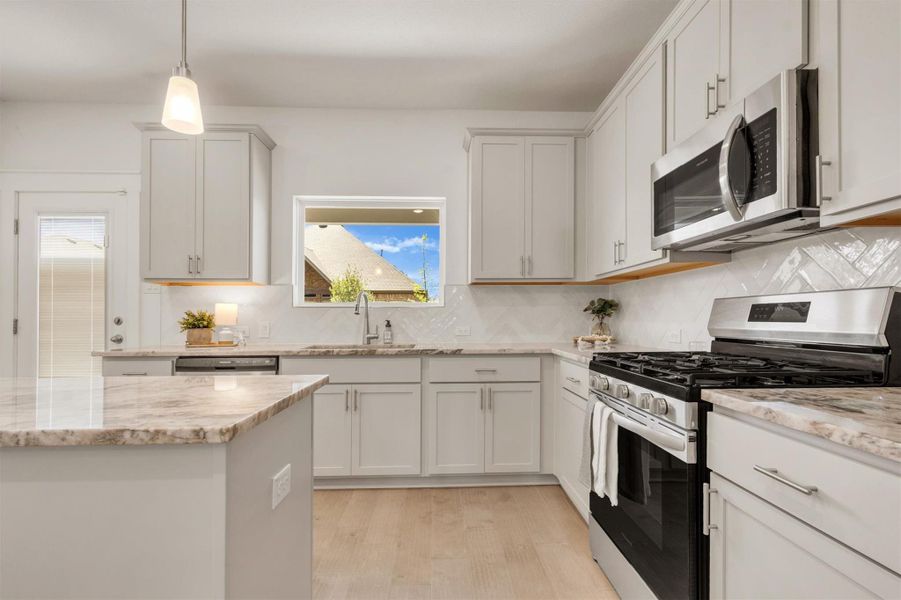 This kitchen features modern stainless steel appliances, light cabinetry, and a stylish backsplash. The space is bright with natural light from a window and glass door, offering a clean and inviting atmosphere.