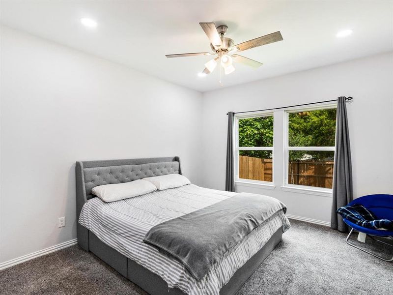 Bright bedroom featuring carpet flooring, a ceiling fan with integrated lighting, recessed overhead lighting, and two windows providing natural light