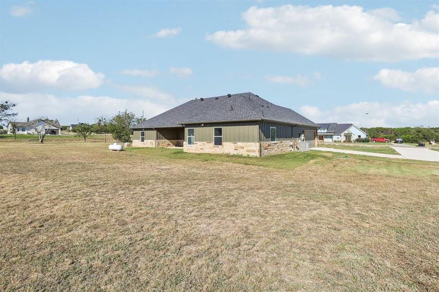 Rear view of property with stone siding, a yard, board and batten siding, and concrete driveway Rear view of property with stone siding, a yard, board and batten siding, and concrete driveway