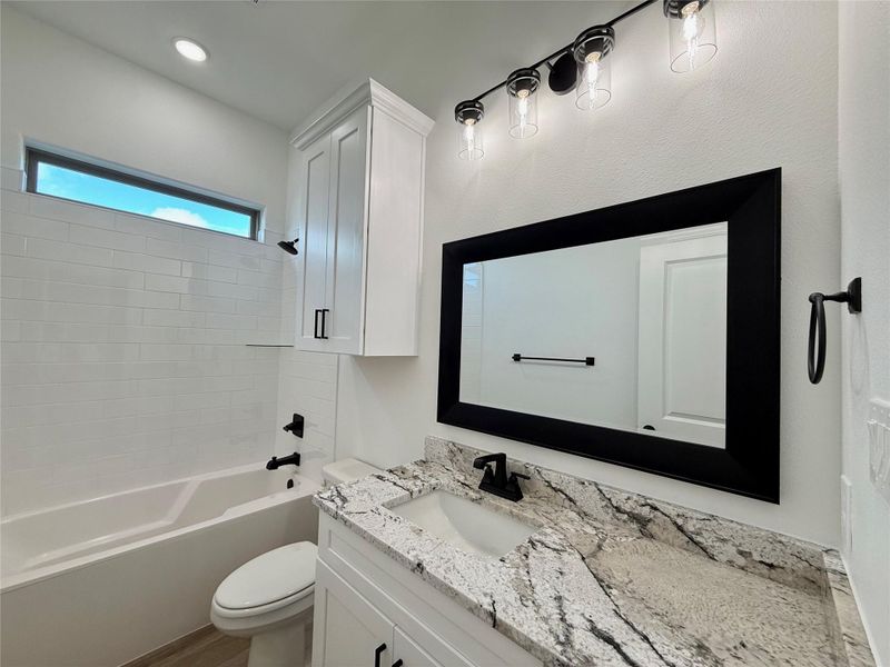 Contemporary bathroom featuring a white subway tile tub surround, white vanity cabinetry with black hardware, and a stone countertop