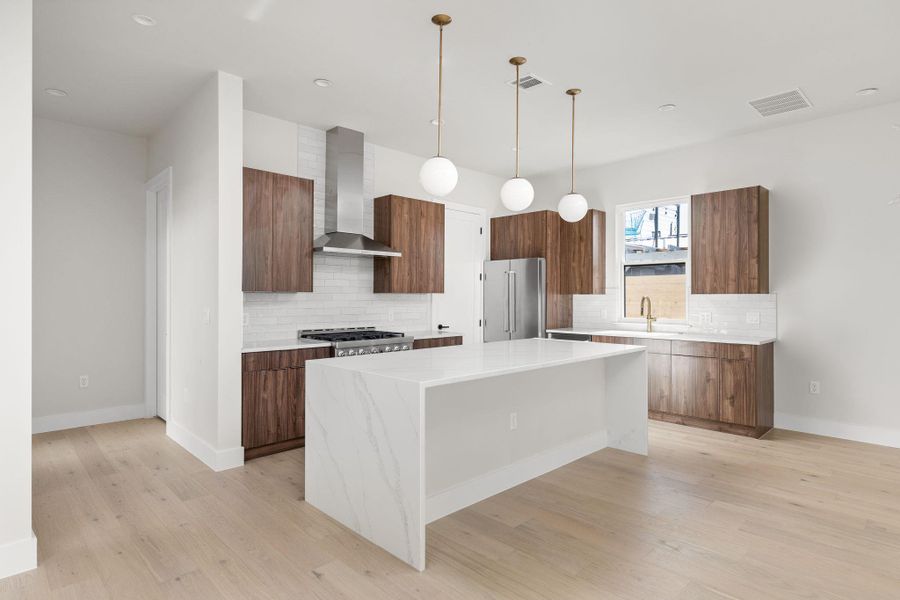 Kitchen with visible vents, a center island, high quality fridge, modern cabinets, and wall chimney exhaust hood