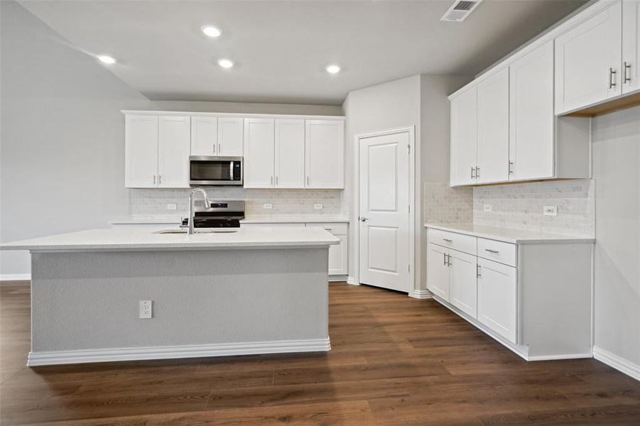 Kitchen with white cabinets, dark wood-type flooring, appliances with stainless steel finishes, and an island with sink