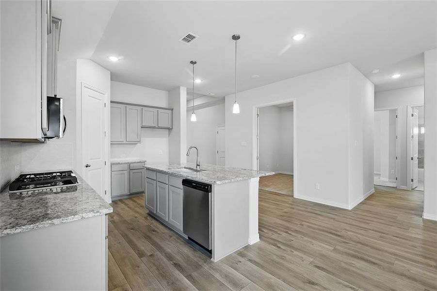 Kitchen featuring light stone countertops, an island with sink, gray cabinetry, and light wood-style floors