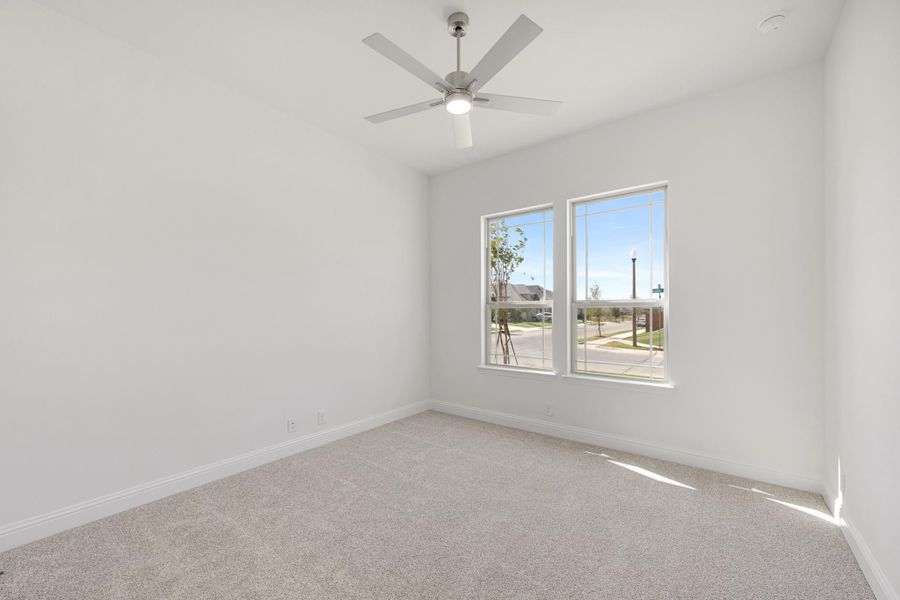 Empty bedroom with carpet flooring, ceiling fan, and two windows overlooking a neighborhood street