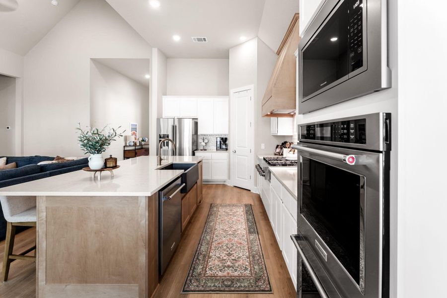 Modern kitchen featuring stainless steel appliances, a wood-finish island with integrated sink, light-toned countertops, and wood-finish flooring