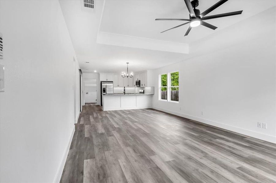 Unfurnished living room featuring ceiling fan with notable chandelier, sink, a tray ceiling, and hardwood / wood-style floors