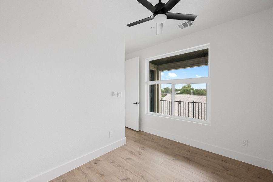 Bright interior space featuring wood-finish flooring, a contemporary ceiling fan, and a large window with a white frame