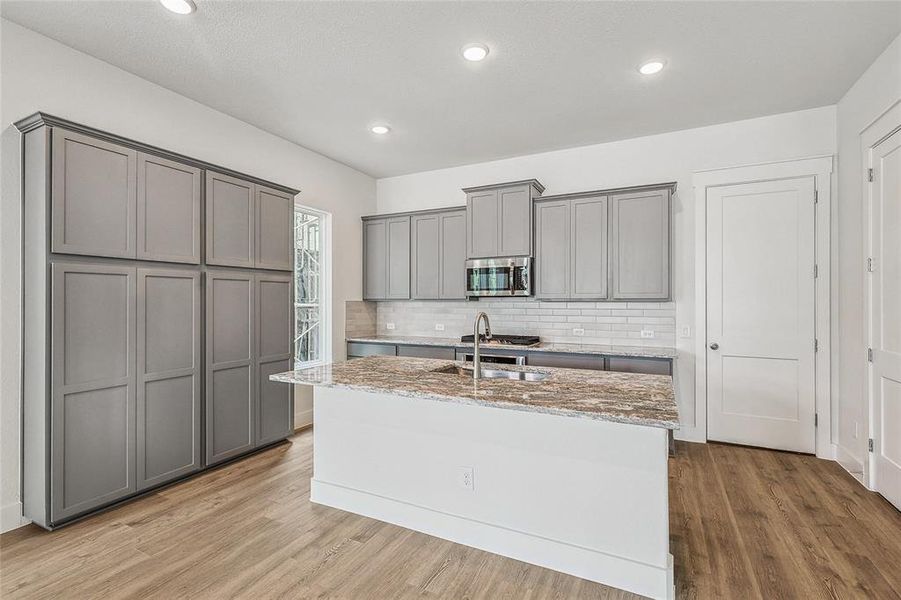 Kitchen with light stone counters, gray cabinets, and light hardwood / wood-style flooring