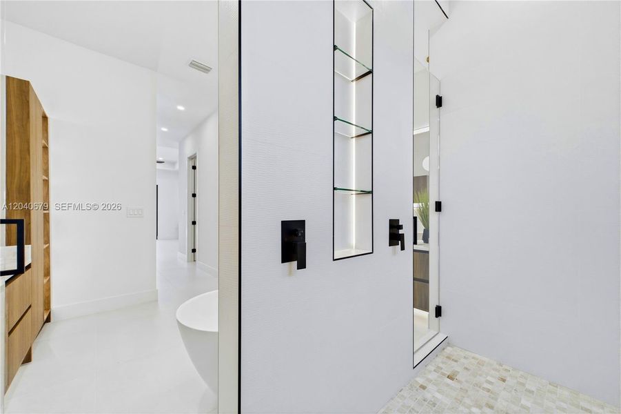 Oversized walk-through shower features dual rainfall showerheads, frameless glass, custom niches, and a sleek open-concept design