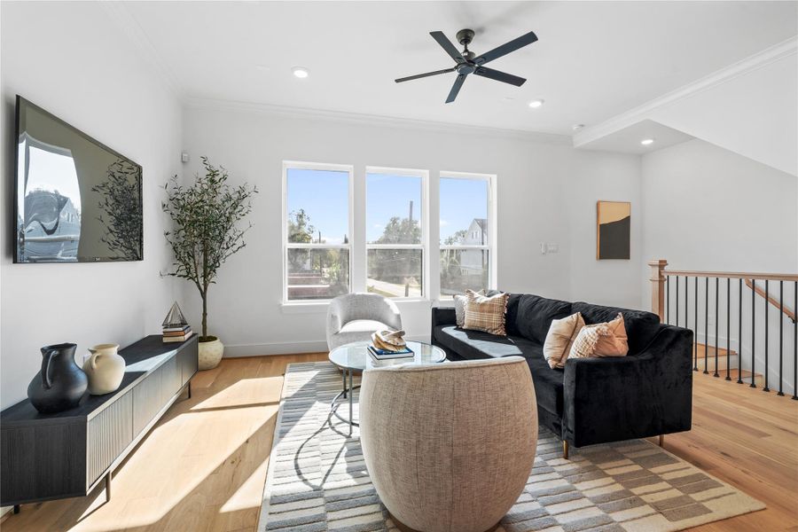 Stairs from the first floor lead into this bright and inviting living room featuring large windows, hardwood floors, and recessed lighting - perfect for relaxing or entertaining.