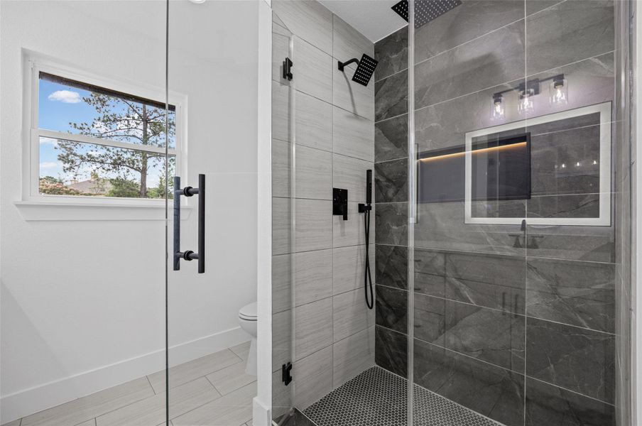 Glass-enclosed shower with dark gray large format tile and a contrasting light gray tiled wall with back-lit niche Glass-enclosed shower with dark gray large format tile and a contrasting light gray tiled wall with back-lit niche
