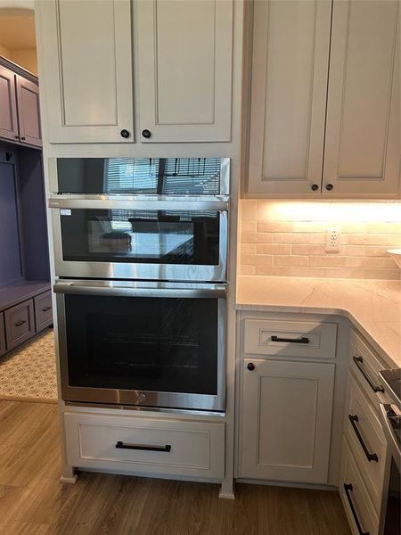 Kitchen featuring a built-in stainless steel oven and microwave combination, light-toned cabinetry with black hardware, stone-finish countertops, and a subway tile backsplash