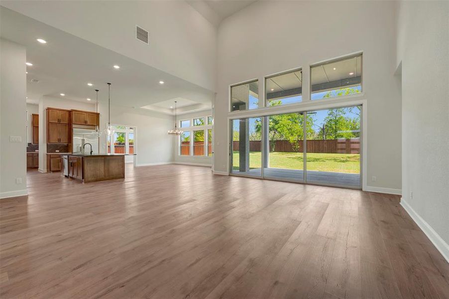 Unfurnished living room featuring suspended lighting, light wood-type flooring, and a high ceiling