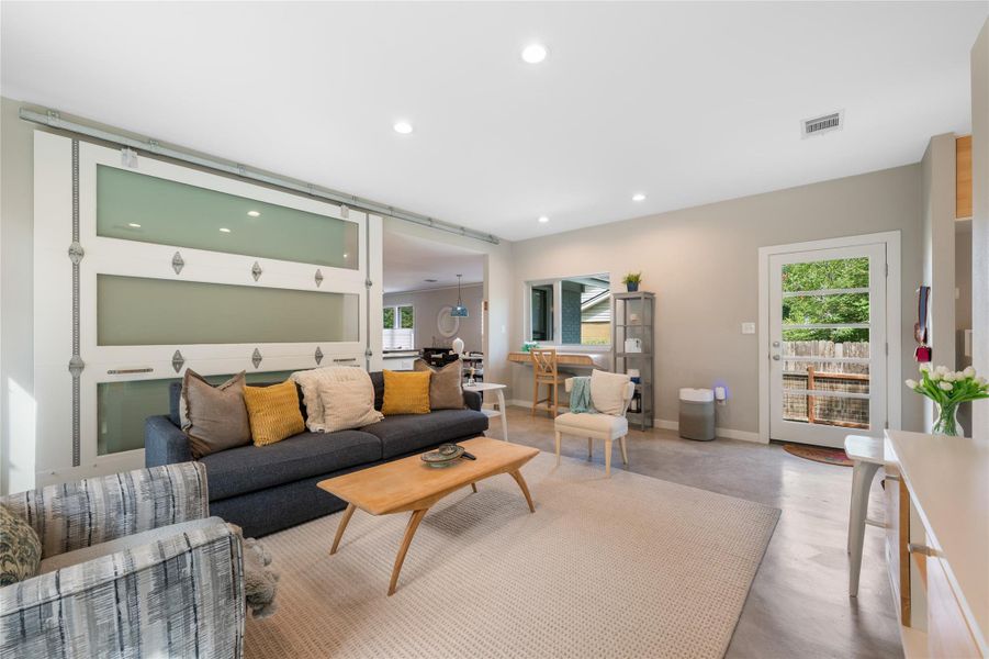 Recessed lighting illuminates this bright, open-plan living space with a stylish barn door separating rooms. Recessed lighting illuminates this bright, open-plan living space with a stylish barn door separating rooms.