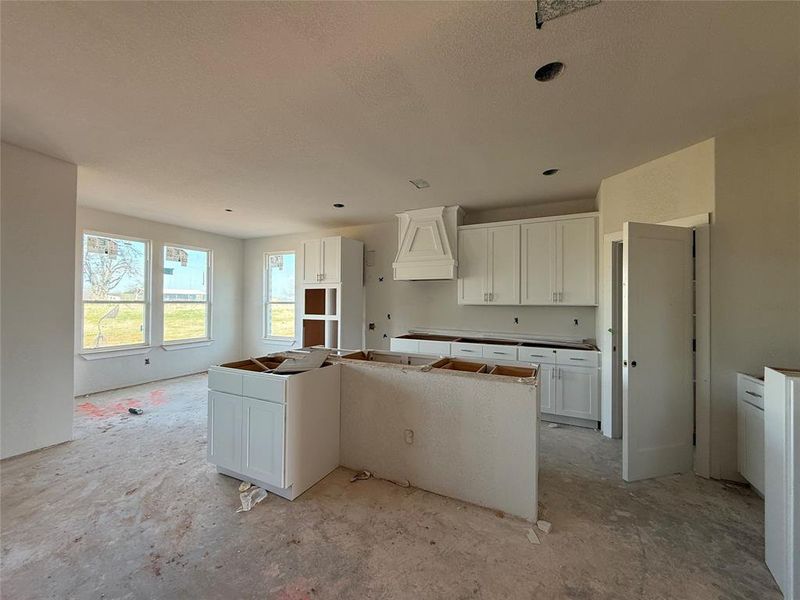 Kitchen with a kitchen island, custom exhaust hood, and white cabinets