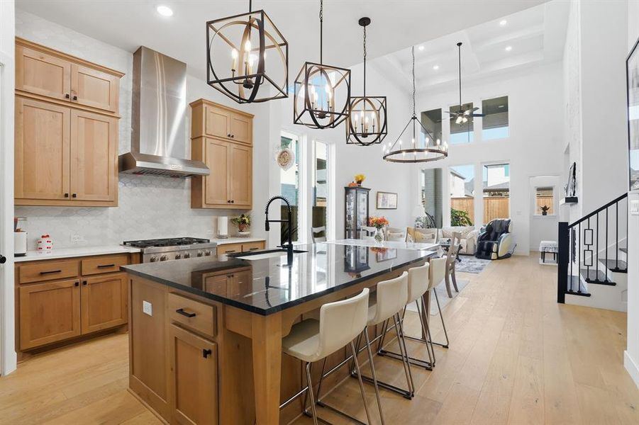 Kitchen featuring decorative backsplash, light wood-type flooring, dark stone counters, a center island with sink, and hanging light fixtures Kitchen featuring decorative backsplash, light wood-type flooring, dark stone counters, a center island with sink, and hanging light fixtures