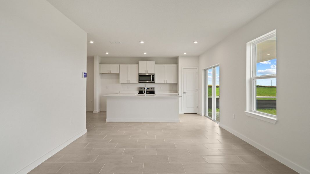 Modern kitchen flows into spacious living area with natural light, tile floors, and backyard views through oversized windows