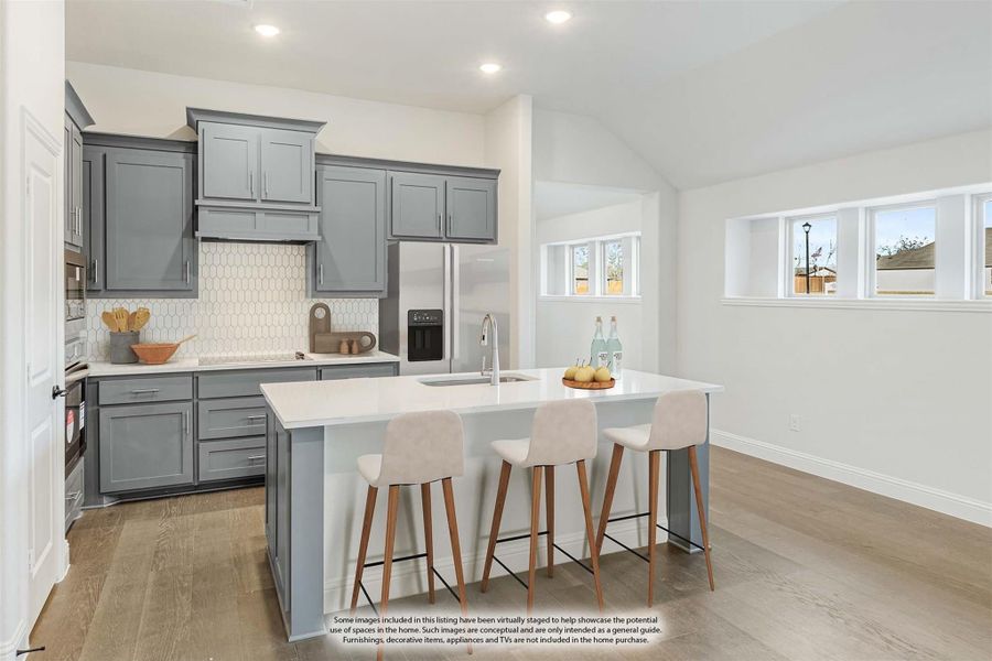 Kitchen with gray cabinets, white hexagon tile backsplash, stainless refrigerator, and island with three bar stools
