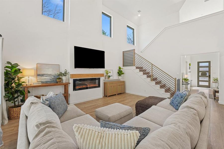 Living area featuring a glass covered fireplace, light wood-style flooring, a high ceiling, recessed lighting, and stairway