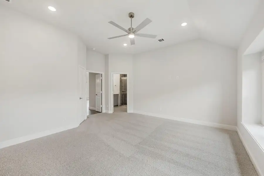 Spacious bedroom with vaulted ceiling, ceiling fan, carpet flooring, and open door to ensuite bathroom Spacious bedroom with vaulted ceiling, ceiling fan, carpet flooring, and open door to ensuite bathroom