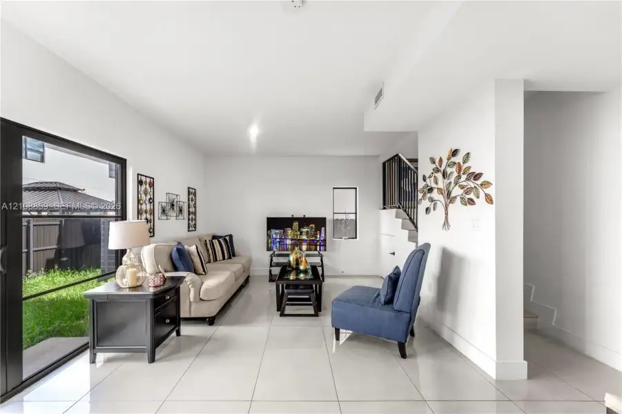 Living area featuring large-format tile flooring, sliding glass door access to the rear exterior, and an open staircase with a metal railing